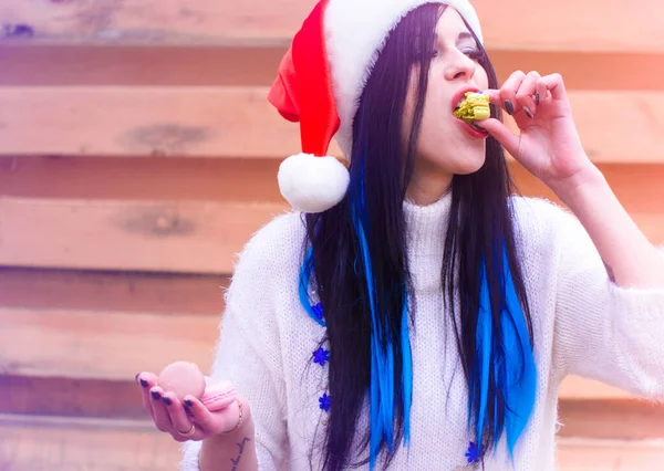 Nice young woman in the New Year\'s cap actively eats sweets and cookies. Rationing sweet in the New Year and Christmas holidays, girls and diet. Harm of sugar on the human body, joy in everyday life