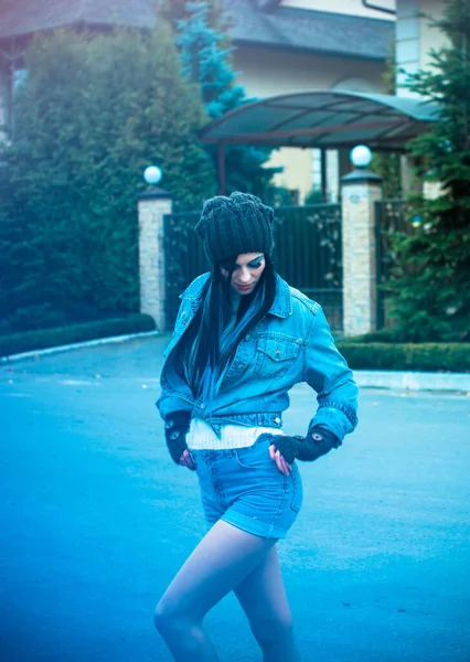 The girl is dressed in a denim jacket and shorts, a white sweater, a knitted hat and gloves. Winter Casual and stylish clothes for European and American winter.