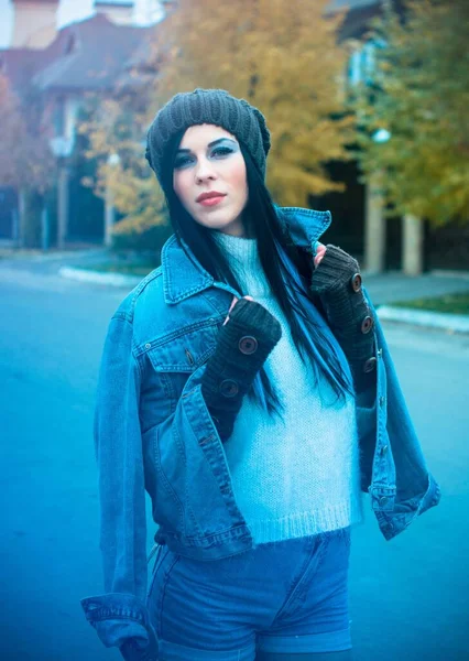 The girl is dressed in a denim jacket and shorts, a white sweater, a knitted hat and gloves. Winter Casual and stylish clothes for European and American winter.