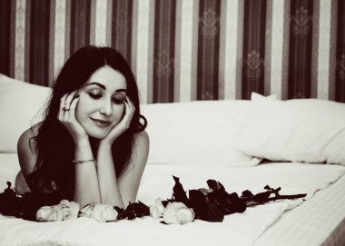 Yatak odasında gül ve romantik ruh hali olan hoş bir kadının fotoğrafı, bugünü kutlayın, kıvırcık saç stili, çekici vücut yatak kadınsı konseptinde poz veriyor.