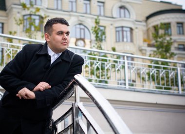 Genç ve cüsseli adam rahatlıyor ve manzaranın tadını çıkarıyor. Büyük şehir yaşamındaki tombul insanlar konsepti. Şehir merkezindeki şişman iş adamının görüntüsü