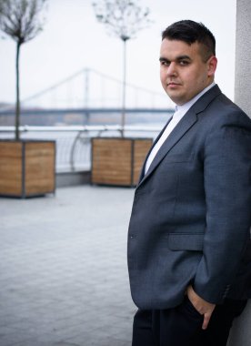 Genç ve cüsseli adam rahatlıyor ve manzaranın tadını çıkarıyor. Büyük şehir yaşamındaki tombul insanlar konsepti. Şehir merkezindeki şişman iş adamının görüntüsü