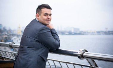 Genç ve cüsseli adam rahatlıyor ve manzaranın tadını çıkarıyor. Büyük şehir yaşamındaki tombul insanlar konsepti. Şehir merkezindeki şişman iş adamının görüntüsü