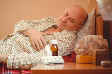 Evde yatakta yatan son sınıf öğrencisi için endişelendim. Yatakta yatan olgun bir adam pijama giyer, acı hisseder, hastalanır..