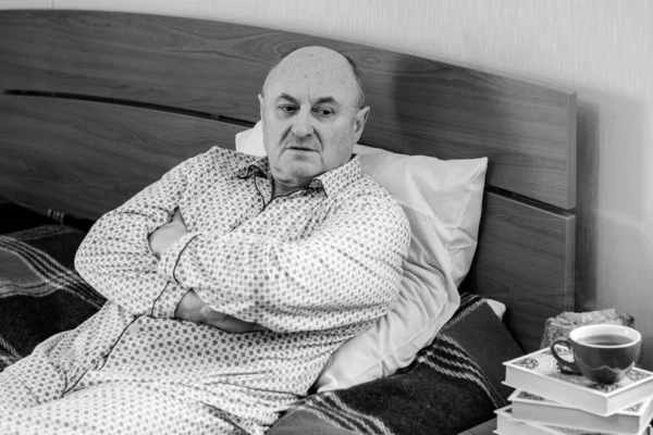 Worried senior lying in bed at home. Mature man lying in bed wear in pajamas, feeling pain, sick.