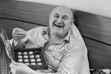 Yaşlı, mutlu, pijamalı bir adam sabahları yatağında çikolata tatlısı yer. Olgun erkeklerin psikolojisi, depresyon ve kötü ruh hallerinden kurtulmak.