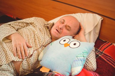 Yaşlı adam rahat bir yerde, yatak odasında oyuncakla pijamalarıyla uyur, emekli olur.