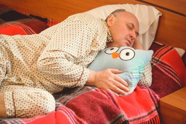 Yaşlı adam rahat bir yerde, yatak odasında oyuncakla pijamalarıyla uyur, emekli olur.