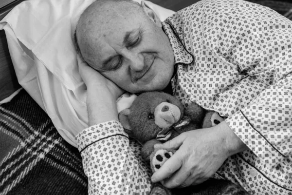 Yaşlı adam rahat bir yerde, yatak odasında oyuncakla pijamalarıyla uyur, emekli olur.