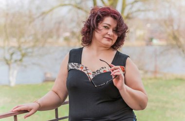 Orta yaşlı ve hayattan zevk alan iri yarı bir kadın. Aşırı kilolu, şık giyinmiş olgun bir bayan. Doğal güzellik.