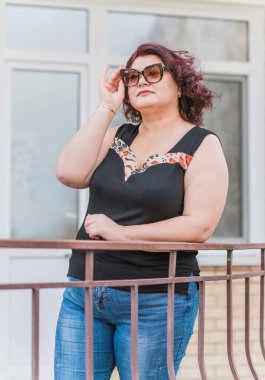 Orta yaşlı ve hayattan zevk alan iri yarı bir kadın. Aşırı kilolu, şık giyinmiş olgun bir bayan. Doğal güzellik.