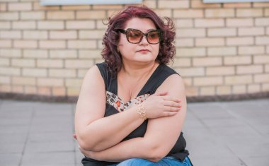 Orta yaşlı ve hayattan zevk alan iri yarı bir kadın. Aşırı kilolu, şık giyinmiş olgun bir bayan. Doğal güzellik.