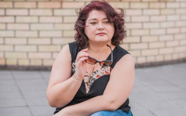 Orta yaşlı ve hayattan zevk alan iri yarı bir kadın. Aşırı kilolu, şık giyinmiş olgun bir bayan. Doğal güzellik.