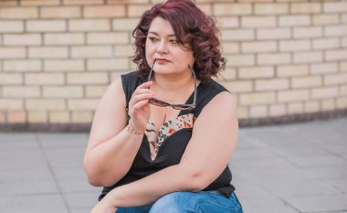 Orta yaşlı ve hayattan zevk alan iri yarı bir kadın. Aşırı kilolu, şık giyinmiş olgun bir bayan. Doğal güzellik.