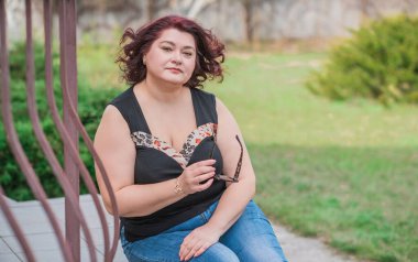 Orta yaşlı ve hayattan zevk alan iri yarı bir kadın. Aşırı kilolu, şık giyinmiş olgun bir bayan. Doğal güzellik.