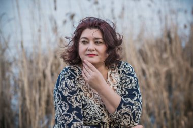 Orta yaşlı ve hayattan zevk alan iri yarı bir kadın. Aşırı kilolu, şık giyinmiş olgun bir bayan. Doğal güzellik.