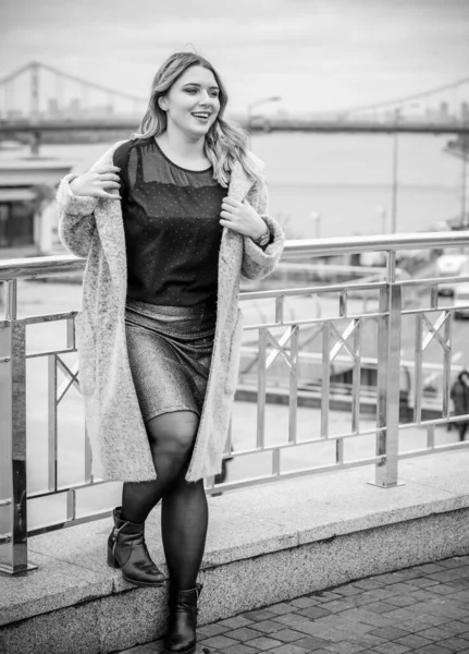 A woman of plus size, American or European appearance walks in the city enjoying life. A young lady with excess weight, stylishly dressed in coat at the center of the city. Natural beauty