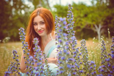 Tarlada açık tenli, güzel kızıl saçlı bir bakire, klasik modaya uygun giyinir. Bir kız çiçeklerin ve otların yanında dinleniyor güzelliğin tadını çıkarıyor.