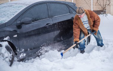 Kış, insanlar ve araba sorunu kavramı. Adam arabayı itmeye çalışıyor, karda sıkışıyor. Karşılıklı yardım. Kış sorunu. Ulaşım, Kış ve Araç Konsepti - Karda sıkışmış arabayı iten adama yakın çekim