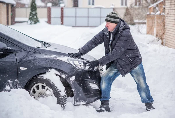 Winter, people and car problem concept. Man try on pushing the car, stuck in the snow. Mutual aid. Winter problem. transportation, winter and vehicle concept - closeup of man pushing car stuck in snow