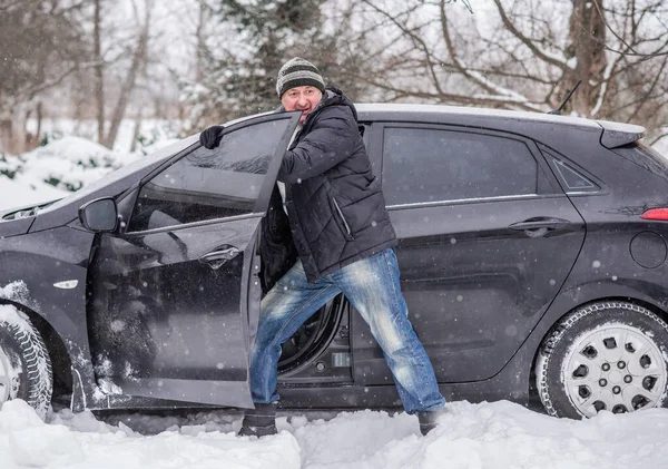 Winter, people and car problem concept. Man try on pushing the car, stuck in the snow. Mutual aid. Winter problem. transportation, winter and vehicle concept - closeup of man pushing car stuck in snow