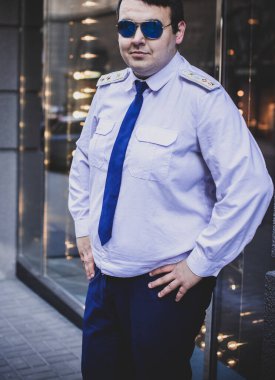 Şehir sokaklarında üniformalı genç ve cüsseli bir adam, tombul insanlar konsepti, büyük şehir hayatı.