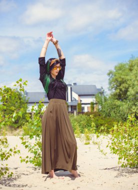 Hippi tarzı ve aksesuarlı genç hippi kadın kuma poz veriyor. Çingene görünümlü boho gezgin kız. Yaz seyahati. Atmosferik hareket ve yeşil kilitli şehvetli portre