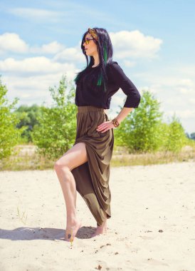 Hippi tarzı ve aksesuarlı genç hippi kadın kuma poz veriyor. Çingene görünümlü boho gezgin kız. Yaz seyahati. Atmosferik hareket ve yeşil kilitli şehvetli portre