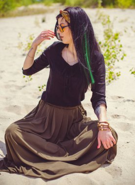 Hippi tarzı ve aksesuarlı genç hippi kadın kuma poz veriyor. Çingene görünümlü boho gezgin kız. Yaz seyahati. Atmosferik hareket ve yeşil kilitli şehvetli portre