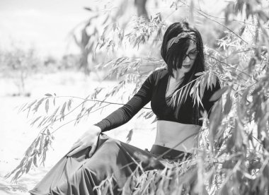 Hippi tarzı ve aksesuarlı genç hippi kadın kuma poz veriyor. Çingene görünümlü boho gezgin kız. Yaz seyahati. Atmosferik hareket ve yeşil kilitli şehvetli portre