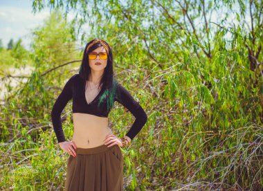 Hippi tarzı ve aksesuarlı genç hippi kadın kuma poz veriyor. Çingene görünümlü boho gezgin kız. Yaz seyahati. Atmosferik hareket ve yeşil kilitli şehvetli portre