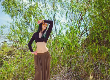 Hippi tarzı ve aksesuarlı genç hippi kadın kuma poz veriyor. Çingene görünümlü boho gezgin kız. Yaz seyahati. Atmosferik hareket ve yeşil kilitli şehvetli portre