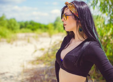 Hippi tarzı ve aksesuarlı genç hippi kadın kuma poz veriyor. Çingene görünümlü boho gezgin kız. Yaz seyahati. Atmosferik hareket ve yeşil kilitli şehvetli portre