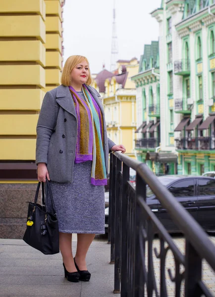 A woman of plus size, American or European appearance walks at city streets enjoying life. A young lady with excess weight, wear a stylish dress. Natural beauty