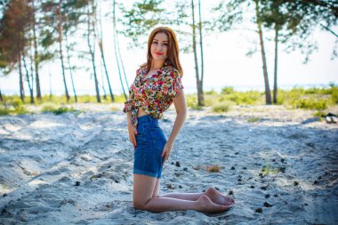 Akşamları, orman, kayalar ve suyun etrafında, kızıl saçlı güzel bir bayan. Klasik tarzda bir portre. Tatlı kadın denizde dinleniyor. Doğada tatil.