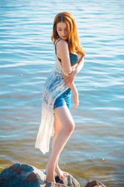 Akşamları, orman, kayalar ve suyun etrafında, kızıl saçlı güzel bir bayan. Klasik tarzda bir portre. Tatlı kadın denizde dinleniyor. Doğada tatil.