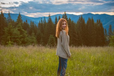 Tatil konsepti. Neşeli kadın uçurumun kenarında dinleniyor ve vadiye ve dağlara bakıyor. Dağlarda seyahat, özgürlük ve aktif yaşam tarzı konsepti