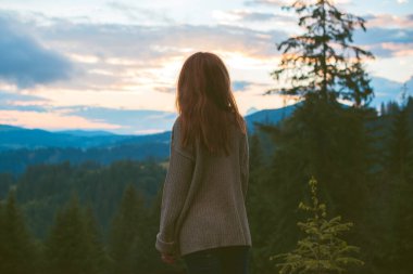 Tatil konsepti. Neşeli kadın uçurumun kenarında dinleniyor ve vadiye ve dağlara bakıyor. Dağlarda seyahat, özgürlük ve aktif yaşam tarzı konsepti