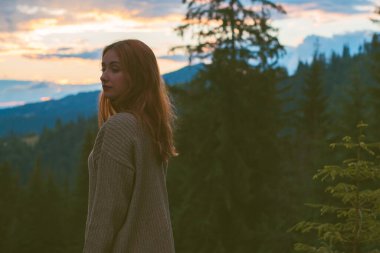 Tatil konsepti. Neşeli kadın uçurumun kenarında dinleniyor ve vadiye ve dağlara bakıyor. Dağlarda seyahat, özgürlük ve aktif yaşam tarzı konsepti