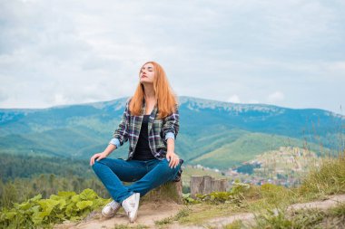 Tatil konsepti. Neşeli kadın uçurumun kenarında dinleniyor ve vadiye ve dağlara bakıyor. Dağlarda seyahat, özgürlük ve aktif yaşam tarzı konsepti