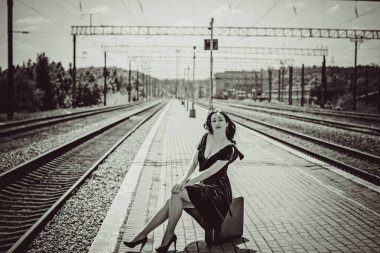 Eski sinema tarzı. Platformda bavulu olan yeşil kadife elbiseli güzel bir kızıl kadın.