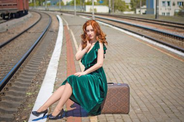 Eski sinema tarzı. Platformda bavulu olan yeşil kadife elbiseli güzel bir kızıl kadın.