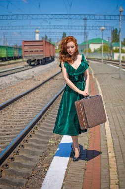 Eski sinema tarzı. Platformda bavulu olan yeşil kadife elbiseli güzel bir kızıl kadın.