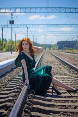 Eski sinema tarzı. Platformda bavulu olan yeşil kadife elbiseli güzel bir kızıl kadın.