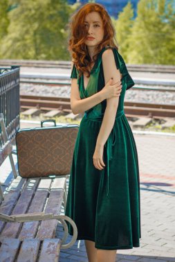 Eski sinema tarzı. Platformda bavulu olan yeşil kadife elbiseli güzel bir kızıl kadın.