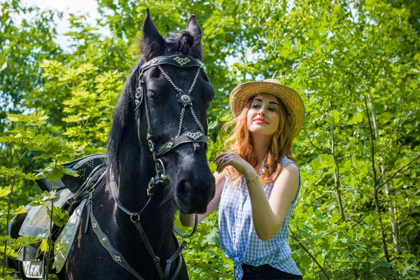 Woman enjoying horse company. Young Beautiful Woman in straw hat With black Horse Outdoors, stylish girl at American country style