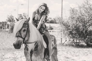 Kırsalda güzel kızıl saçlı bir kız ve bir atı var. Güzel bir binici ve at. At çiftliğinde sanat fotoğrafçılığı. Sonbaharda kırsal alanda ata binen çekici bir kız.