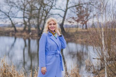 Menekşe ceketli bir kadın, renkli bir atkı, şehir parkında güzel bir sarışın kadın portresi, modaya uygun bir konsept.