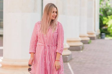 Büyük bedenli, Amerikan ya da Avrupa görünümlü mutlu bir kadın şehirde hayatın tadını çıkarıyor. Aşırı kilolu genç bir bayan, şehir parkında şık giyinmiş. Doğal güzellik.