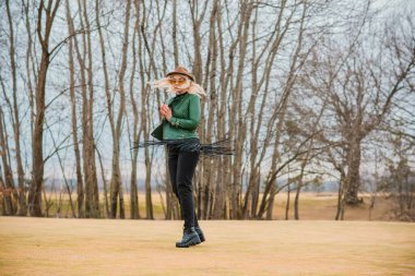 Kadın, eko-deri yeşil ceket, Fedora kahverengi şapka ve eski model havacı gözlükleri giyiyor, püsküllü kemer, moda konsept. 